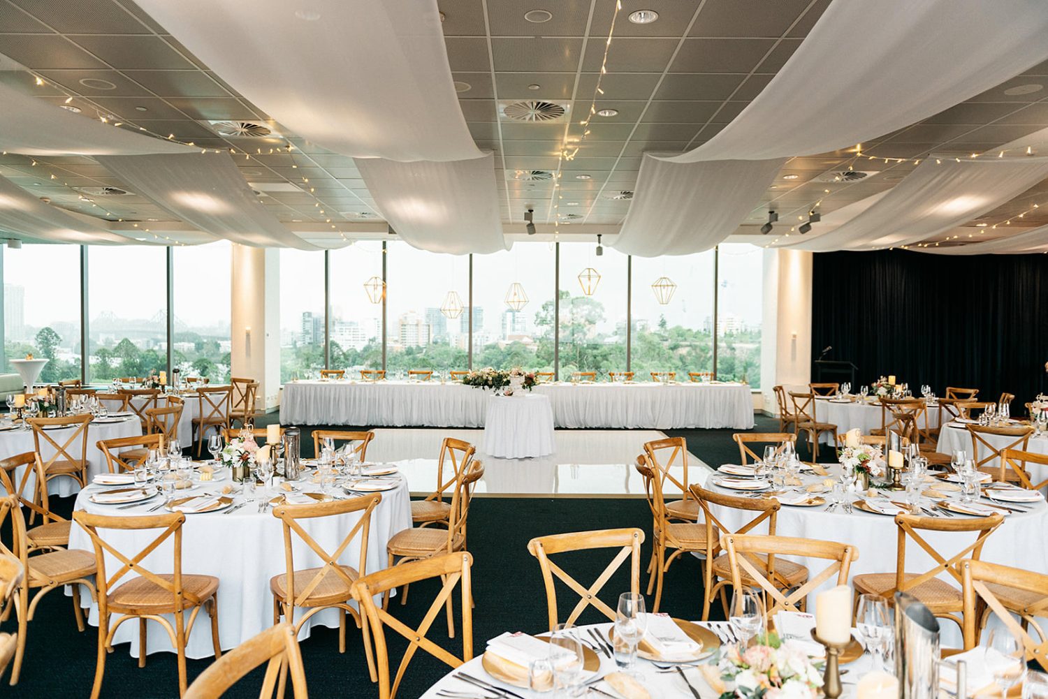 Round wedding tables with dark linen and white florals overlooking the city at Room Three Sixty