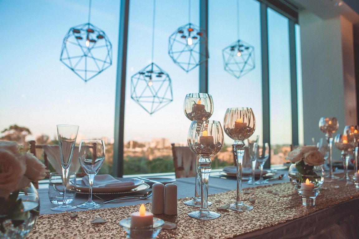 A styled Room Three Sixty wedding table at golden hour with geometric pendant lights, glassware and a sequinned runner overlooking Brisbane